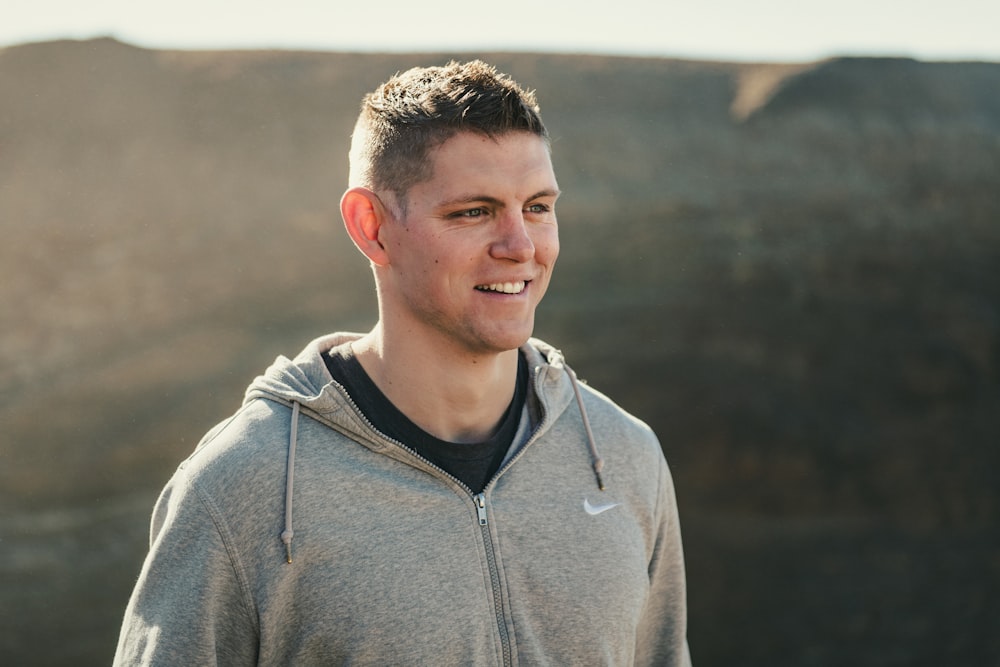 a man in a gray hoodie standing in front of a mountain