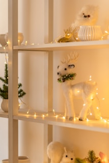 A decorative shelf is adorned with festive items including a fluffy white owl, a white reindeer adorned with fairy lights, and a small faux pine tree in a pot. The warm lighting creates a cozy and inviting atmosphere.
