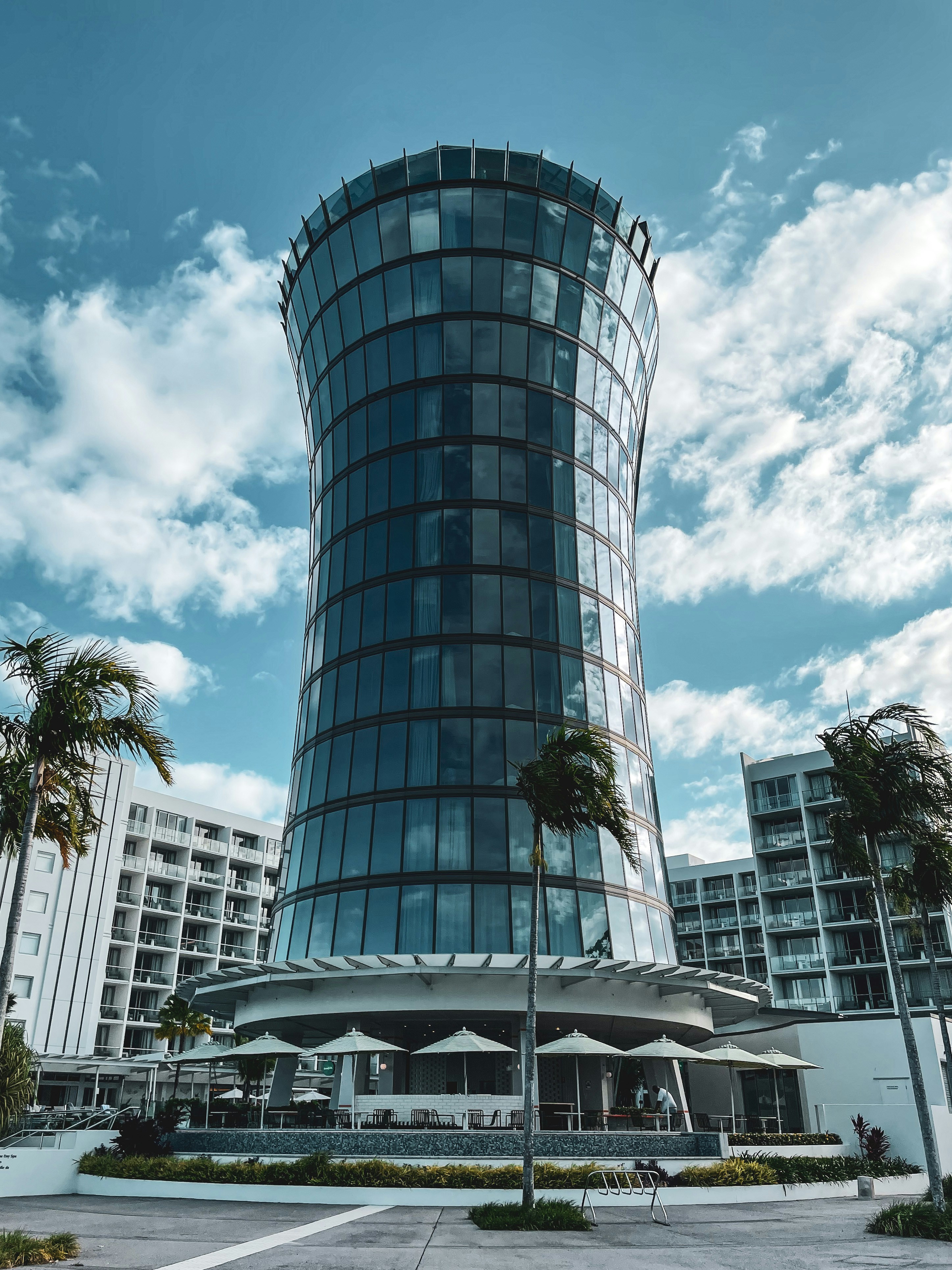 a tall glass building with palm trees in front of it