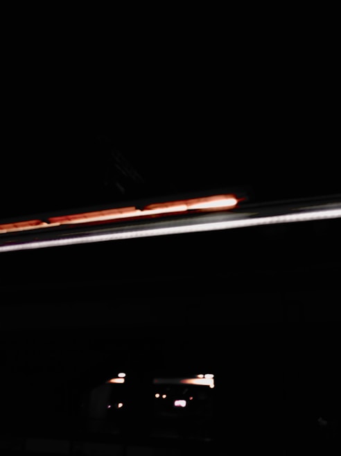 A dark, abstract scene with minimal lighting, featuring horizontal lines of orange and white light against a black background, creating a mysterious and moody atmosphere.