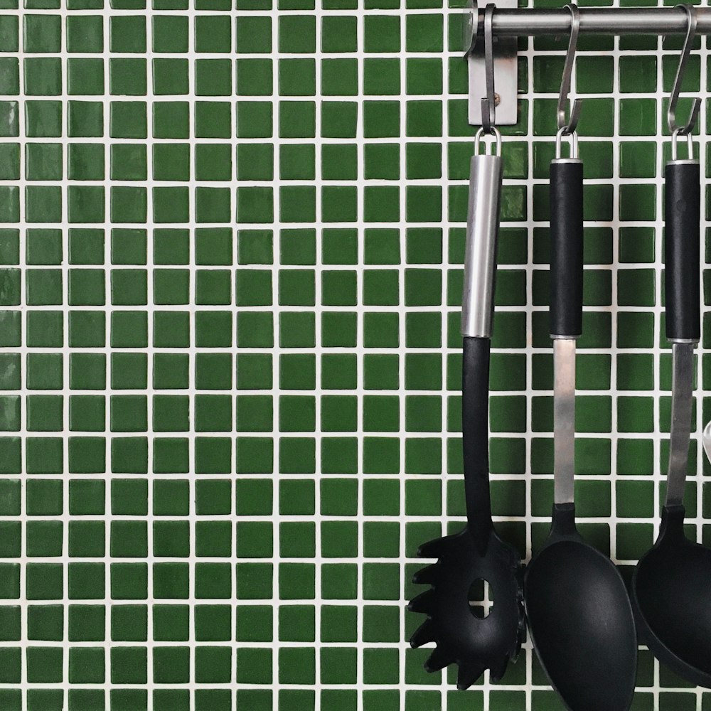 a green tiled wall with spoons and spatulas hanging from hooks