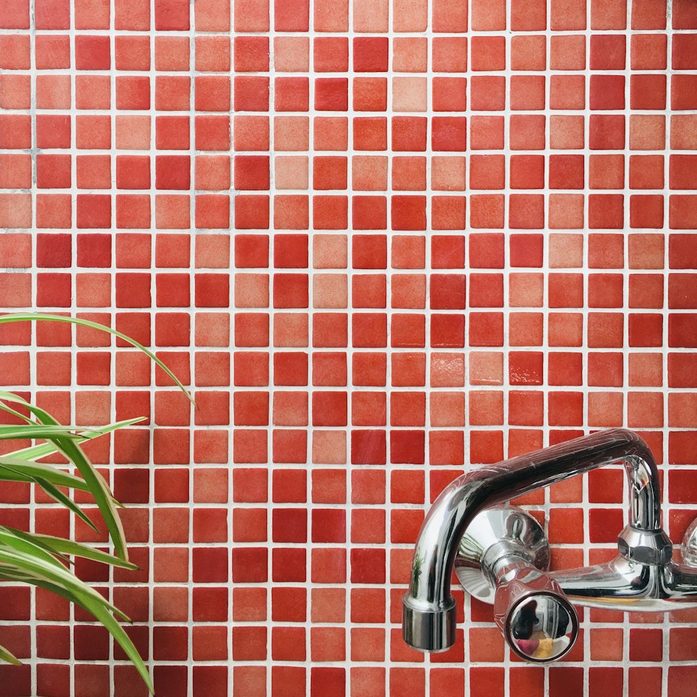 a red tiled wall with a chrome faucet