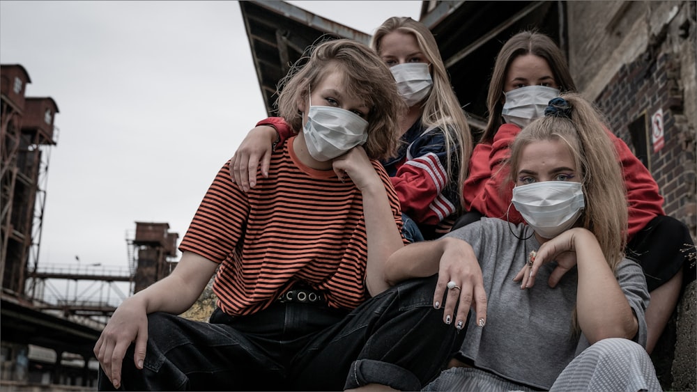 a group of girls wearing face masks sitting on a ledge