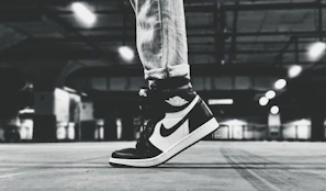 Street scene featuring a figure in monochrome streetwear with clean lines and polished sneakers, framed by soft natural light.