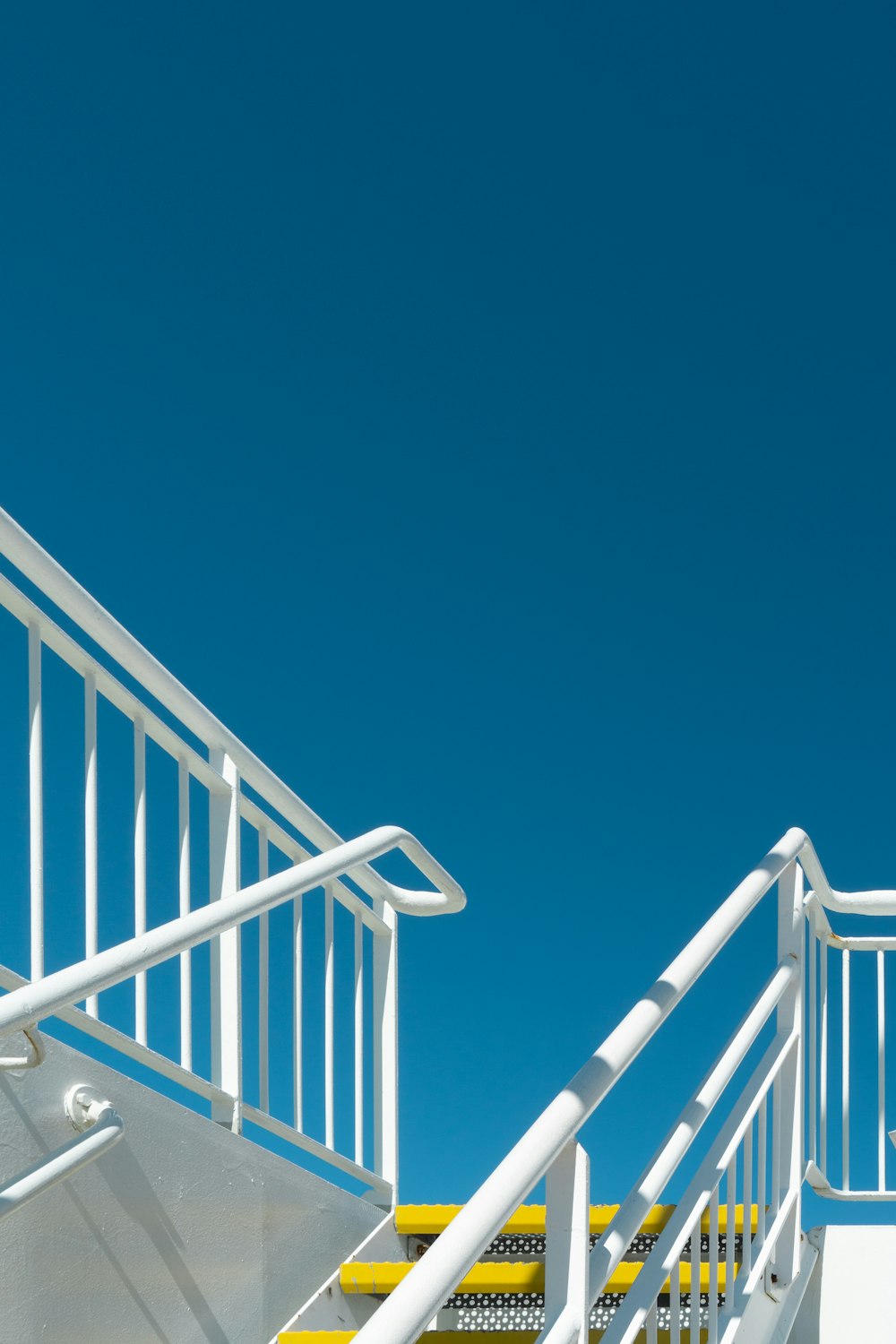 a white staircase with yellow railings against a blue sky