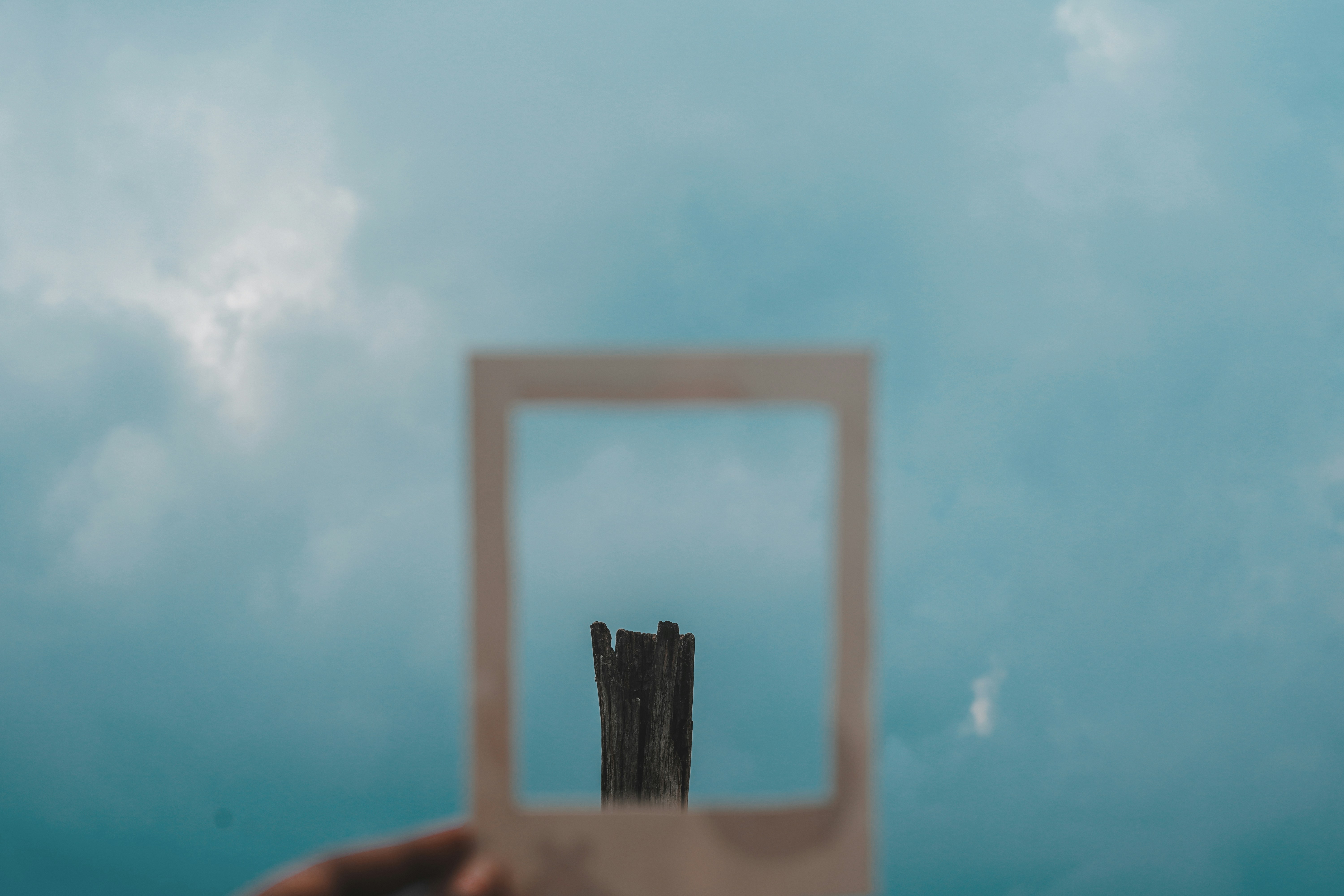 a hand holding a square object in front of a cloudy sky, 