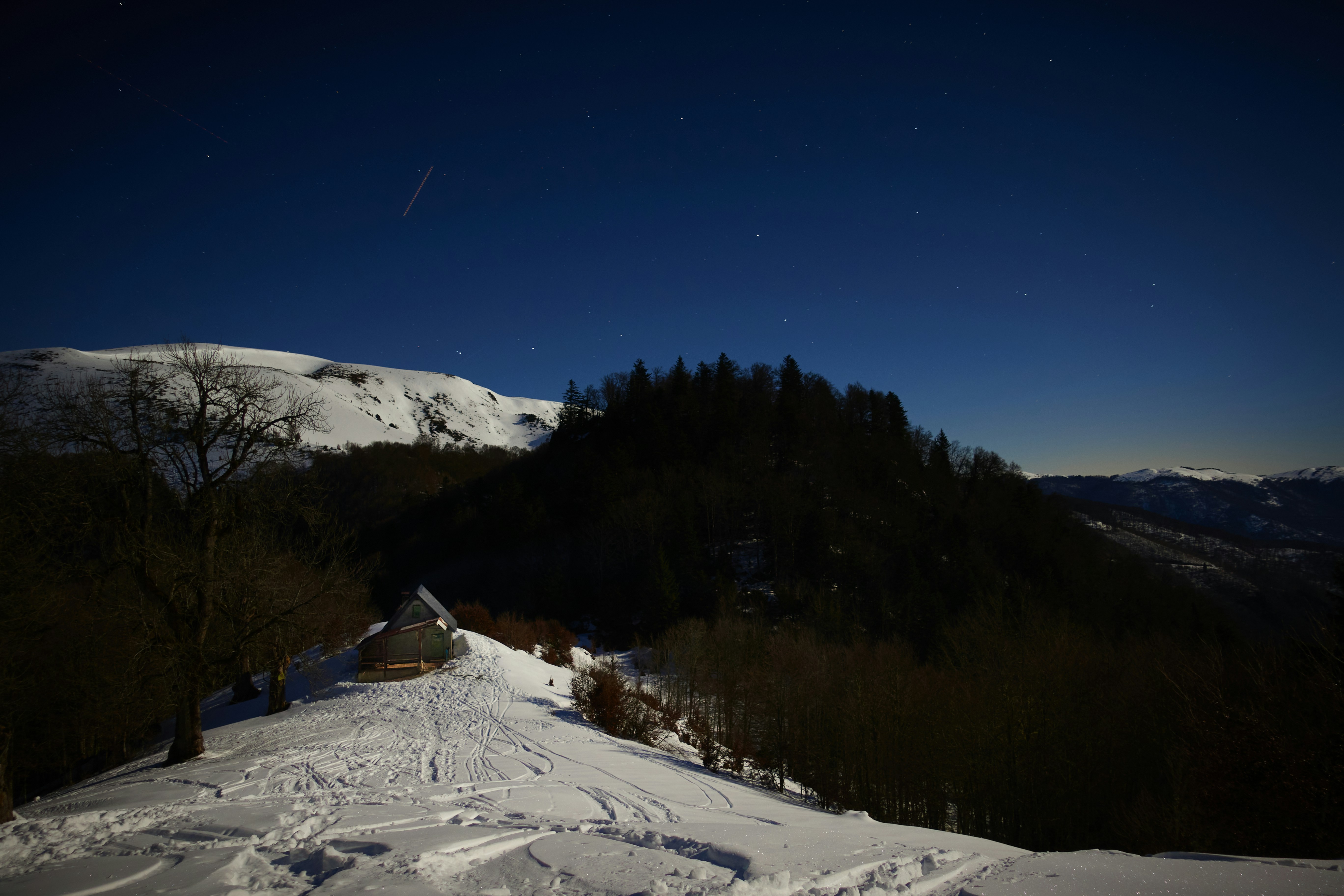 a snow covered hill with a house on top of it, A hut in the Pyrénées by a bright night