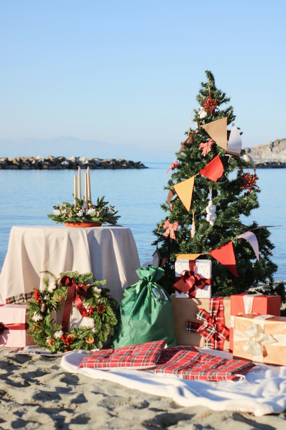 uma árvore de Natal na praia com presentes sob ela