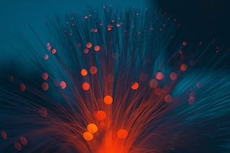 Bright, glowing orange and red lights spread out in radial patterns against a dark blue background, resembling fiber optic cables or light trails.