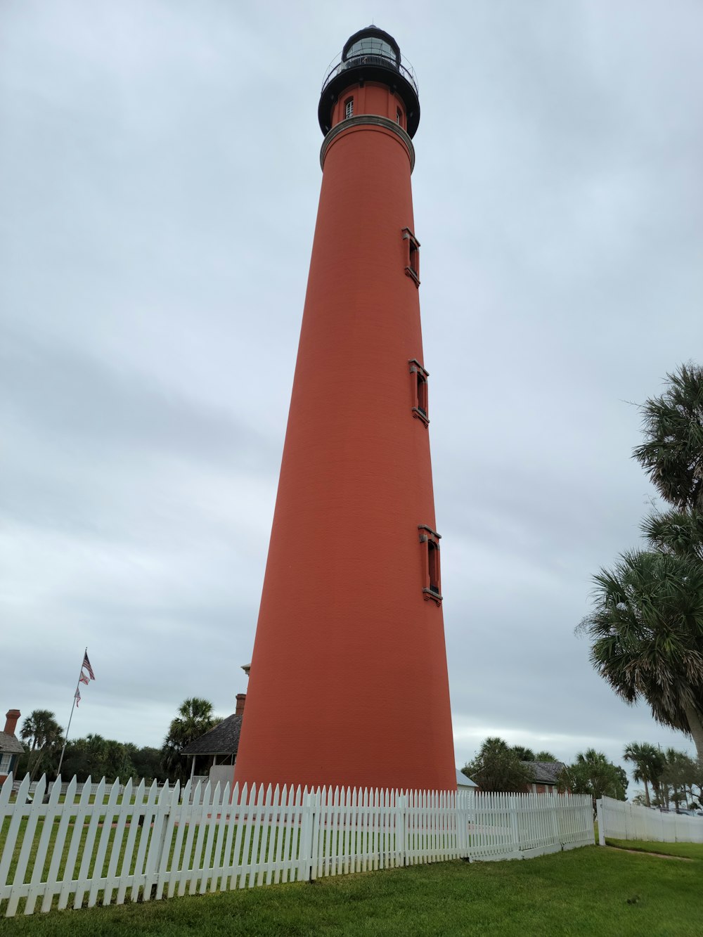 a tall red light house sitting next to a white picket fence
