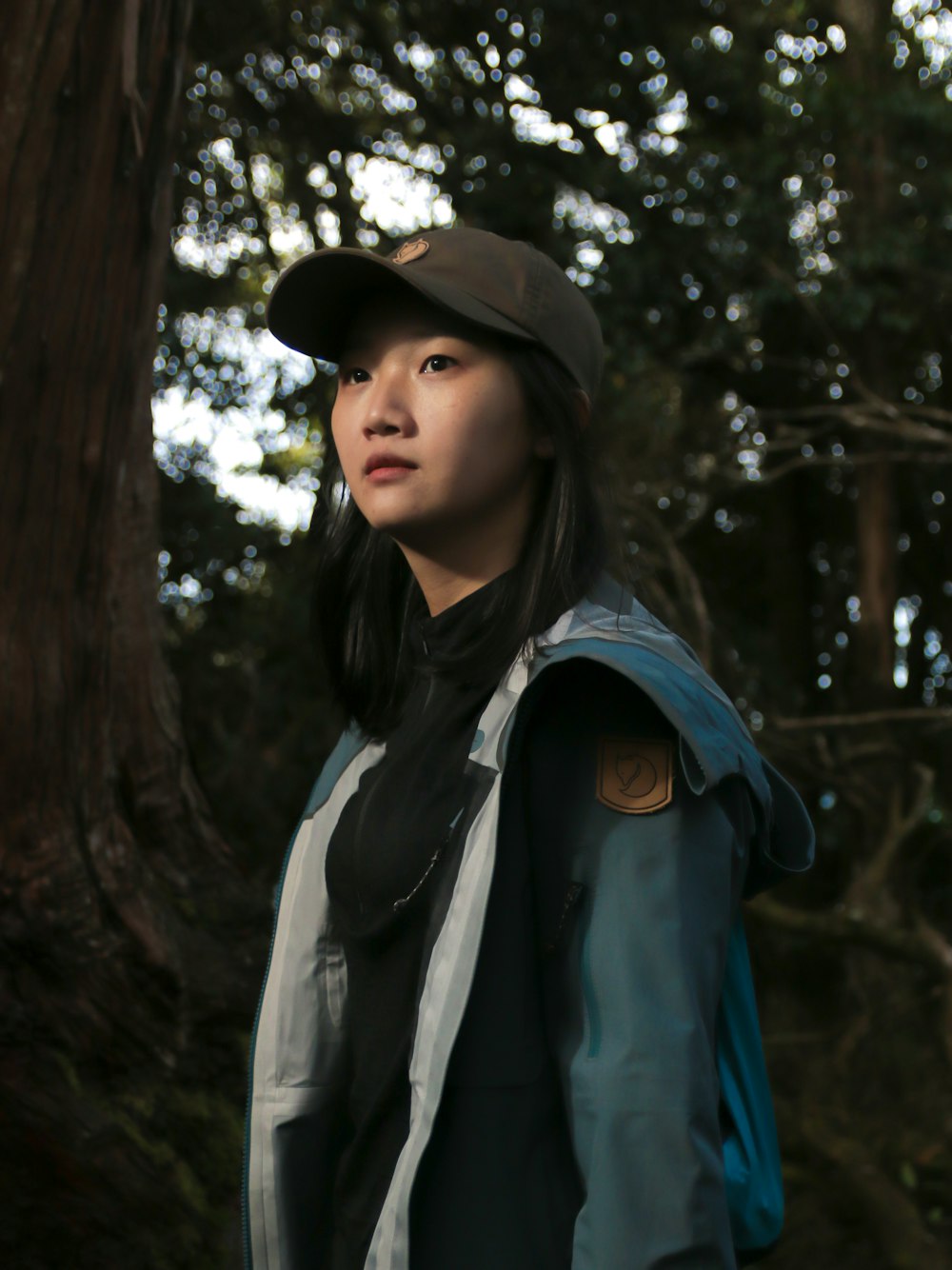 a woman standing in front of a tree wearing a hat