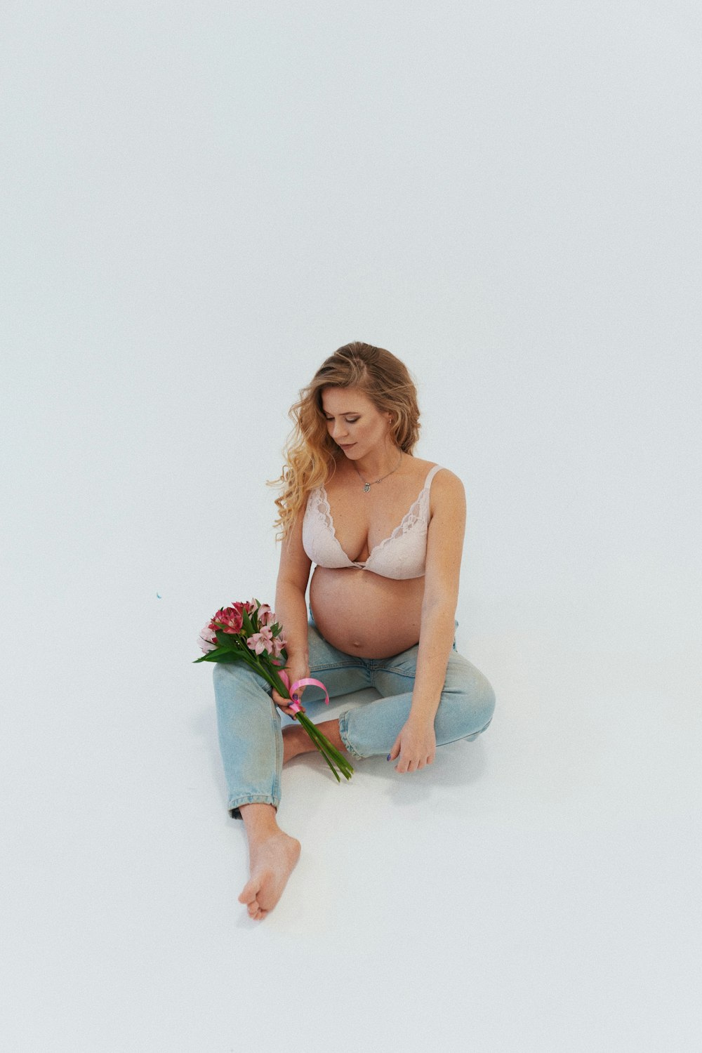 a pregnant woman sitting on the ground with a bouquet of flowers