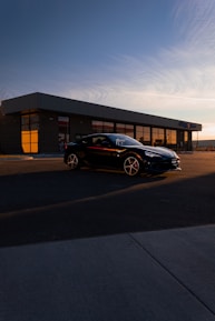 A sleek black car parked in front of a modern building at sunset