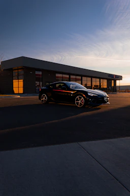 A sleek black luxury limo parked outside a modern airport terminal at sunset.