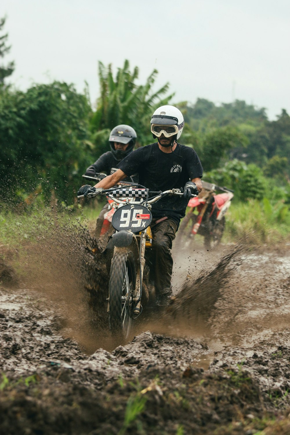 two people riding dirt bikes on a muddy road
