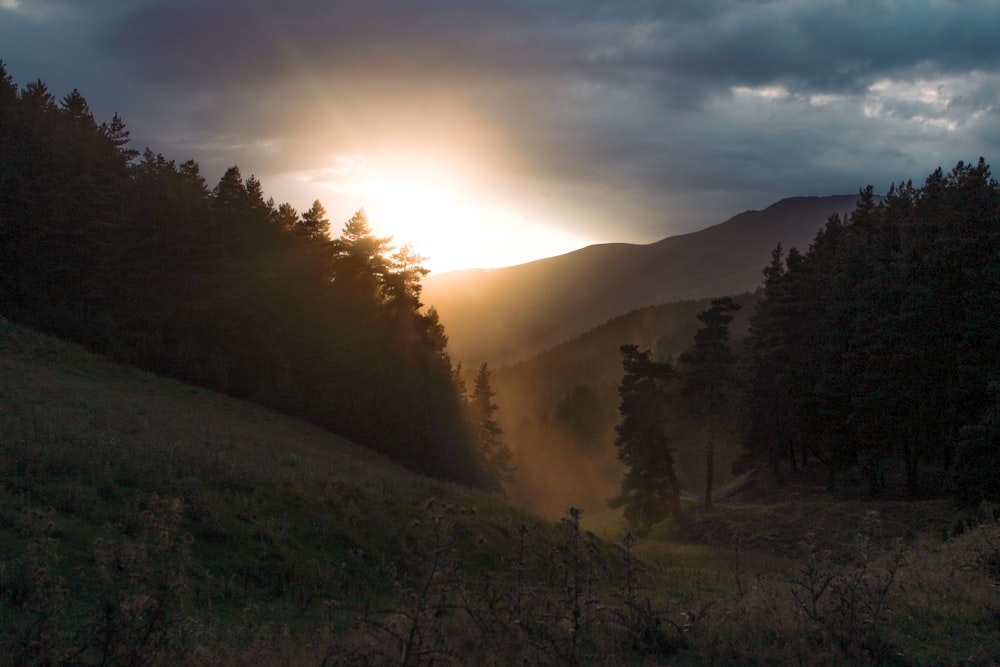 the sun is shining through the clouds in the mountains