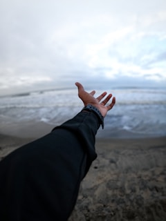 a person's hand reaching out towards the ocean