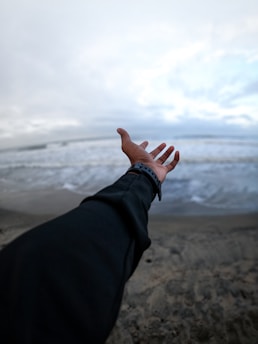 a person's hand reaching out towards the ocean
