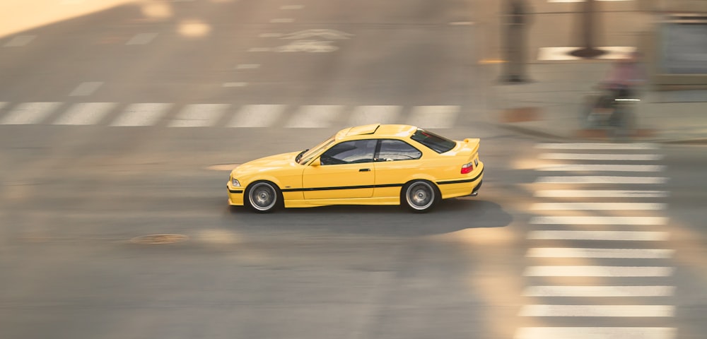 a yellow car driving down a street next to a cross walk