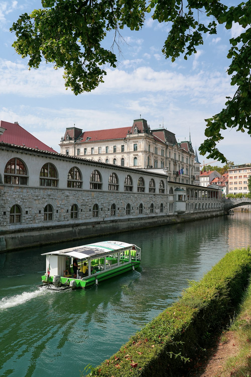 Un barco verde que viaja río abajo junto a edificios altos