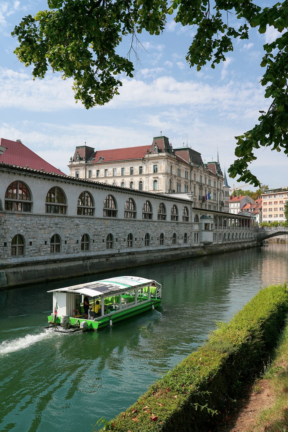 a green boat traveling down a river next to tall buildings