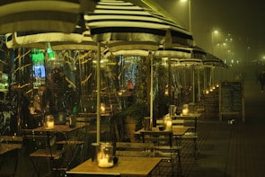 An elegant café terrace with cream umbrellas and muted gold accents, softly lit in the early evening.
