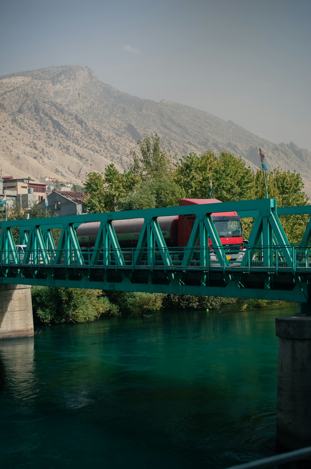 a red bus is crossing a bridge over a river