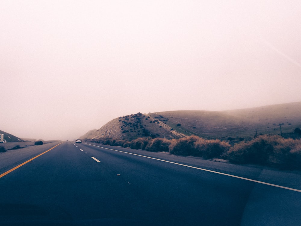 a car driving down a road next to a lush green hillside