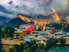 a rainbow shines in the sky over a mountain village