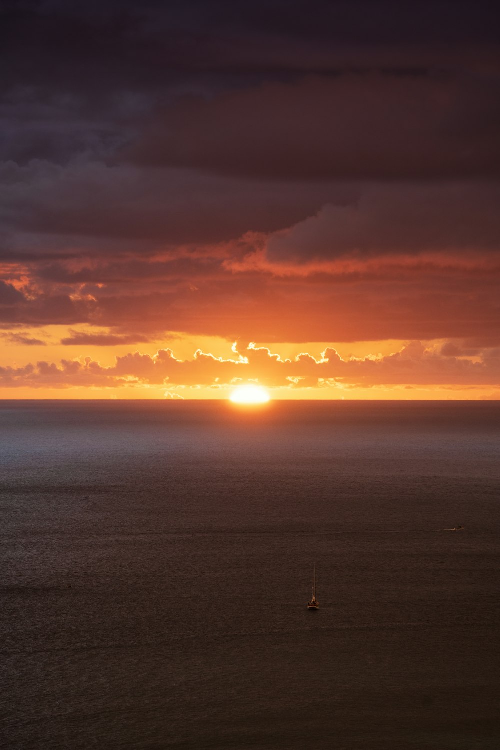 the sun is setting over the ocean with a sailboat in the foreground