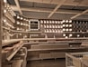 A well-organized display of various lighting fixtures, including wall-mounted lamps, spotlights, and ceiling lights, arranged on a dark wall. Shelves beneath the lights hold boxed products, and a few price tags are visible. The setting appears to be a store showroom with a focus on lighting solutions.