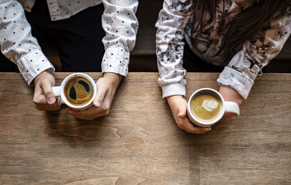 two people holding cups of coffee on top of a wooden table