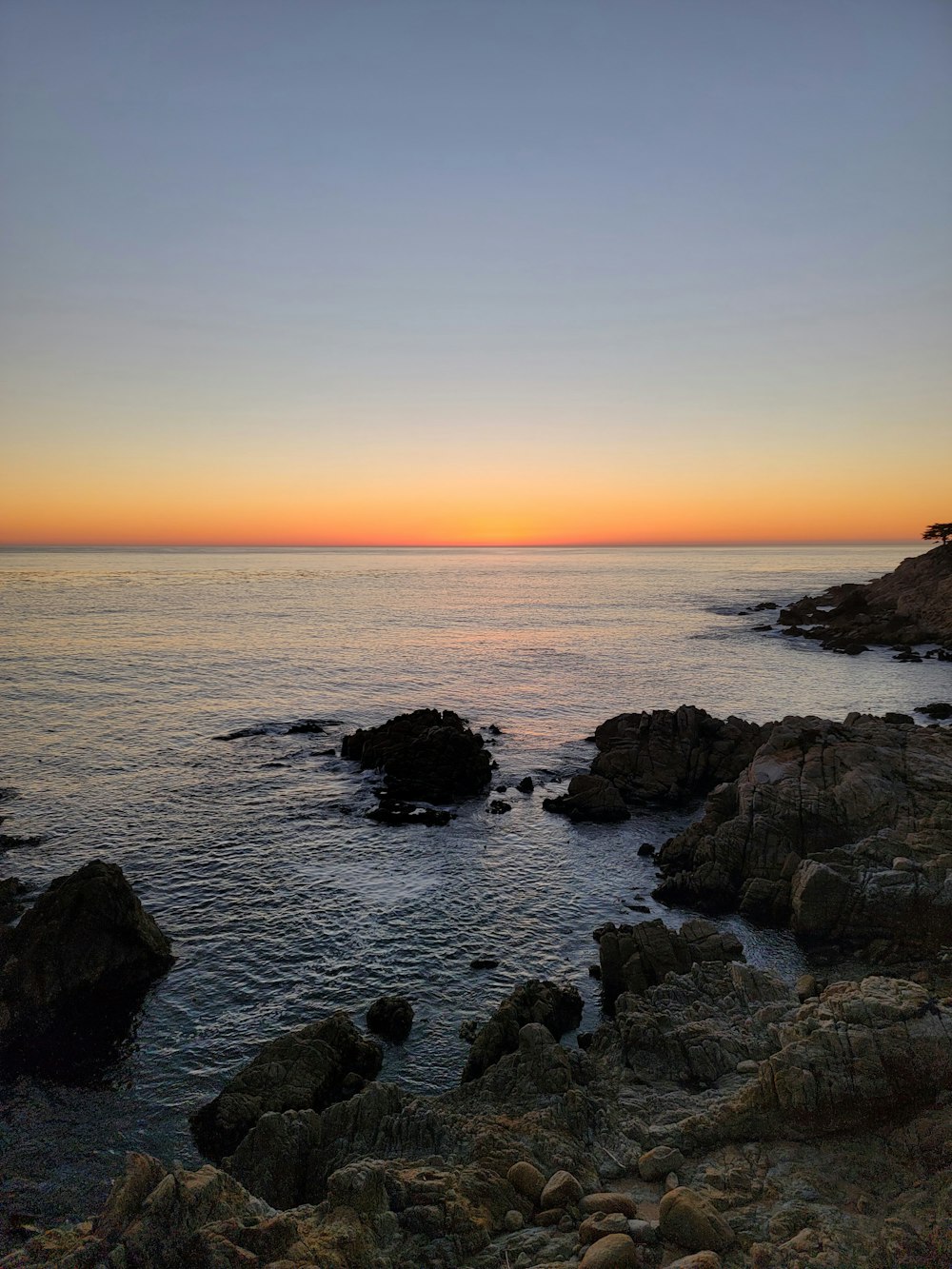 the sun is setting over the ocean and rocks