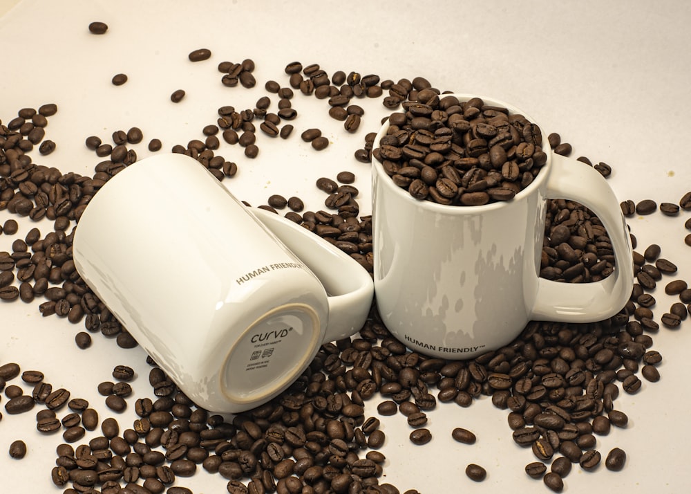 two coffee mugs sitting on top of a pile of coffee beans