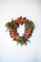 A delicate wreath woven from pinecones, native flowers, and greenery resting on a rustic wooden table.