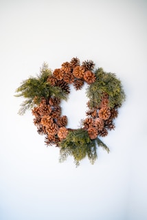 A delicate wreath woven from pinecones, native flowers, and greenery resting on a rustic wooden table.