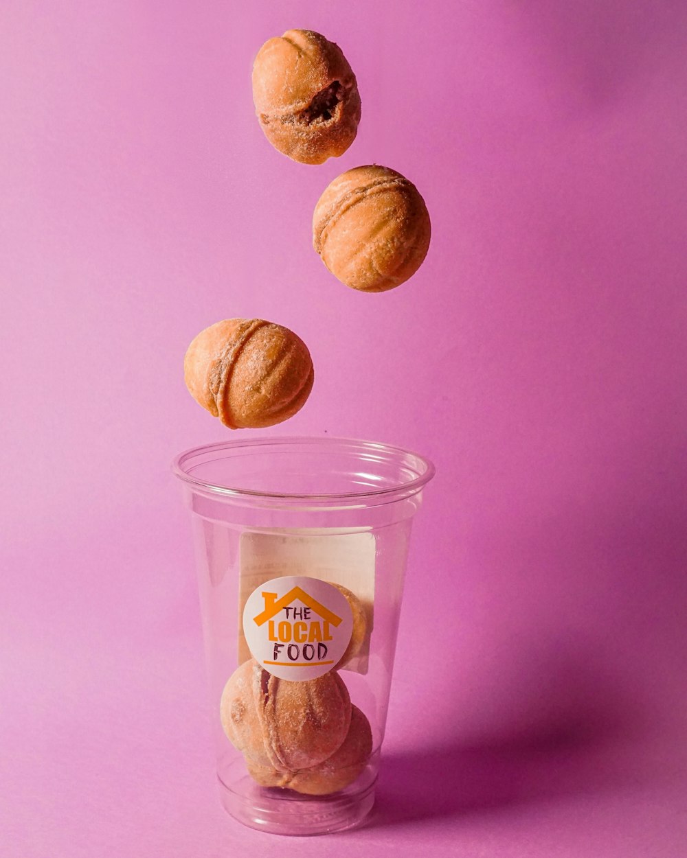 a plastic cup filled with doughnuts on top of a purple background