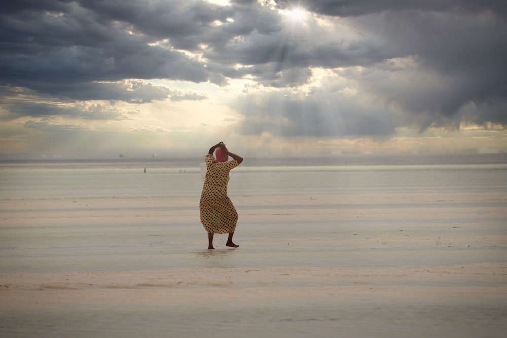 a woman in a dress standing on a beach under a cloudy sky