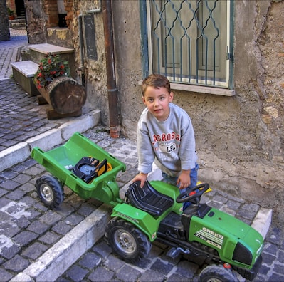 A smiling kid holding a small wrench, sitting beside a vintage tractor.