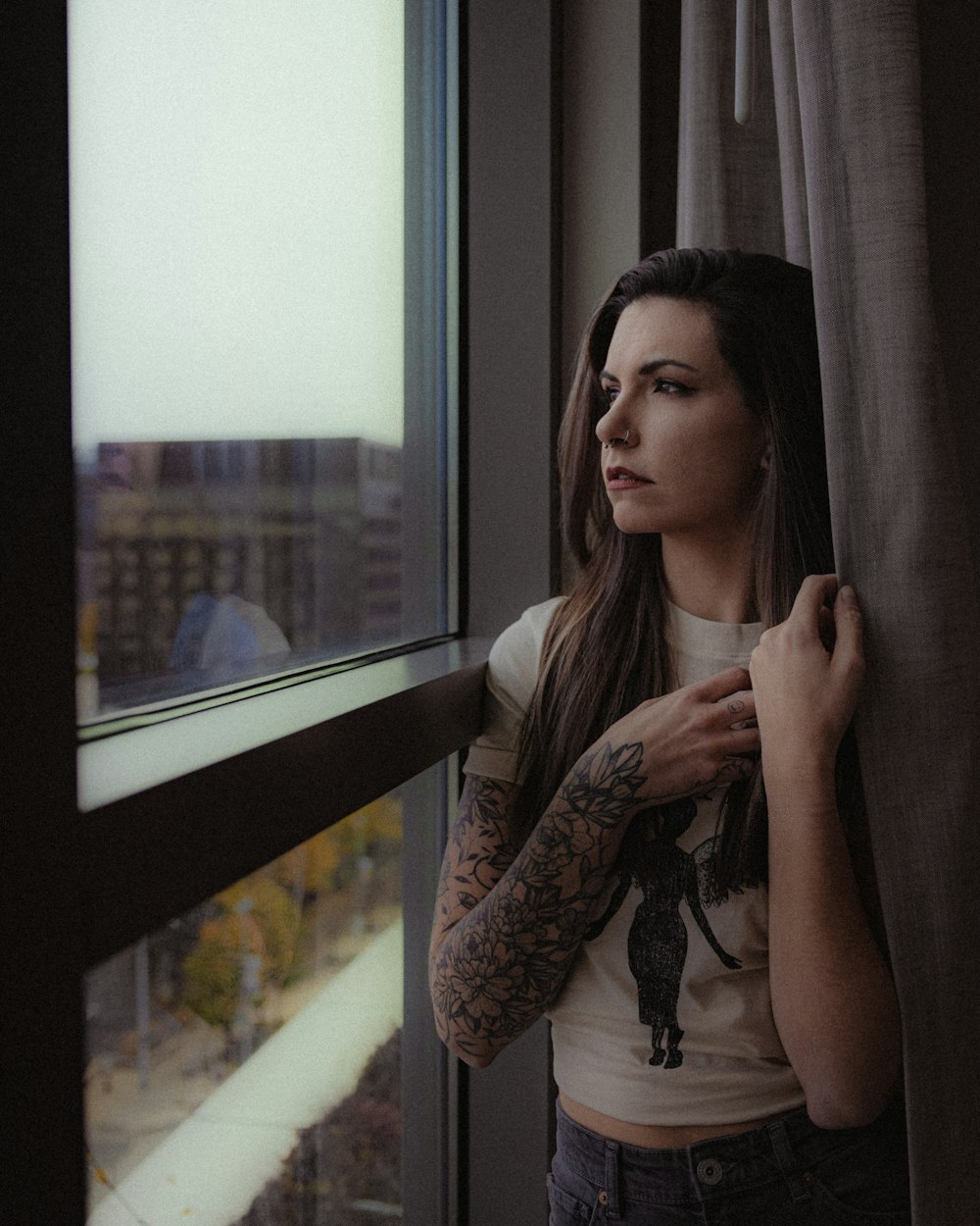 a woman standing next to a window with a tattoo on her arm