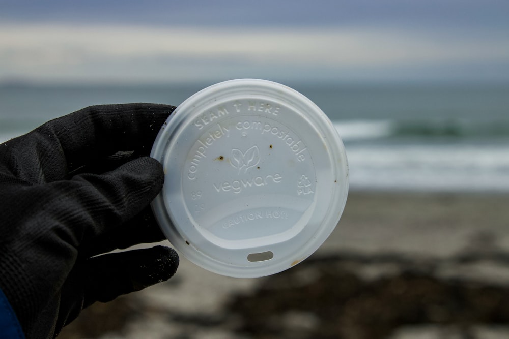 a hand holding a plastic cup with a beach in the background