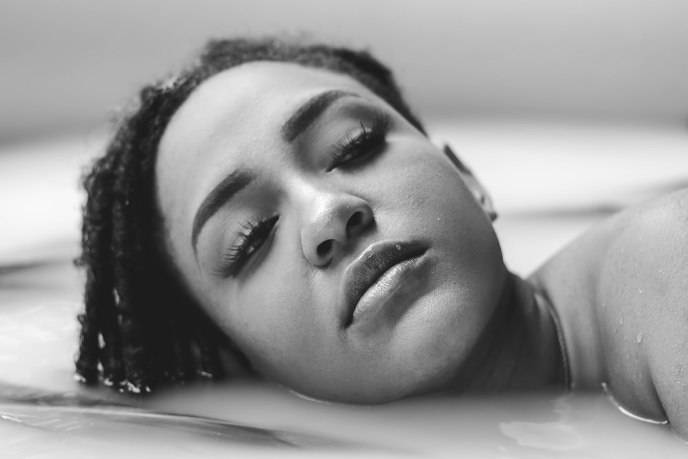 a woman laying down in a bathtub with her eyes closed