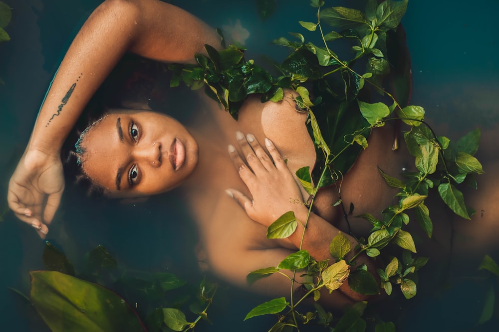 a woman laying in a pool of water surrounded by greenery