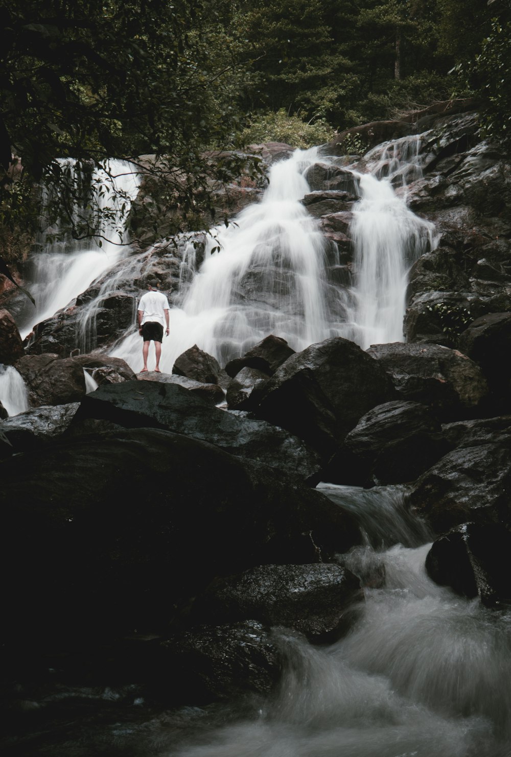 a person standing on a rock in front of a waterfall