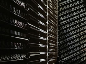 A dark room filled with rows of server racks illuminated by tiny lights and reflections. The metallic surfaces create a sense of symmetry and order, while the low light adds a mysterious ambiance.