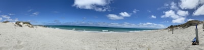 A panoramic view of a white sandy beach with deep blue ocean waves on a sunny day