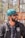 A person with a beard and sunglasses is wearing a turquoise headscarf and a jacket with a logo that reads 'Northeast United FC'. The individual appears to be outside, under natural light, with a blurred background of trees and structures.