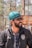 A person with a beard and sunglasses is wearing a turquoise headscarf and a jacket with a logo that reads 'Northeast United FC'. The individual appears to be outside, under natural light, with a blurred background of trees and structures.