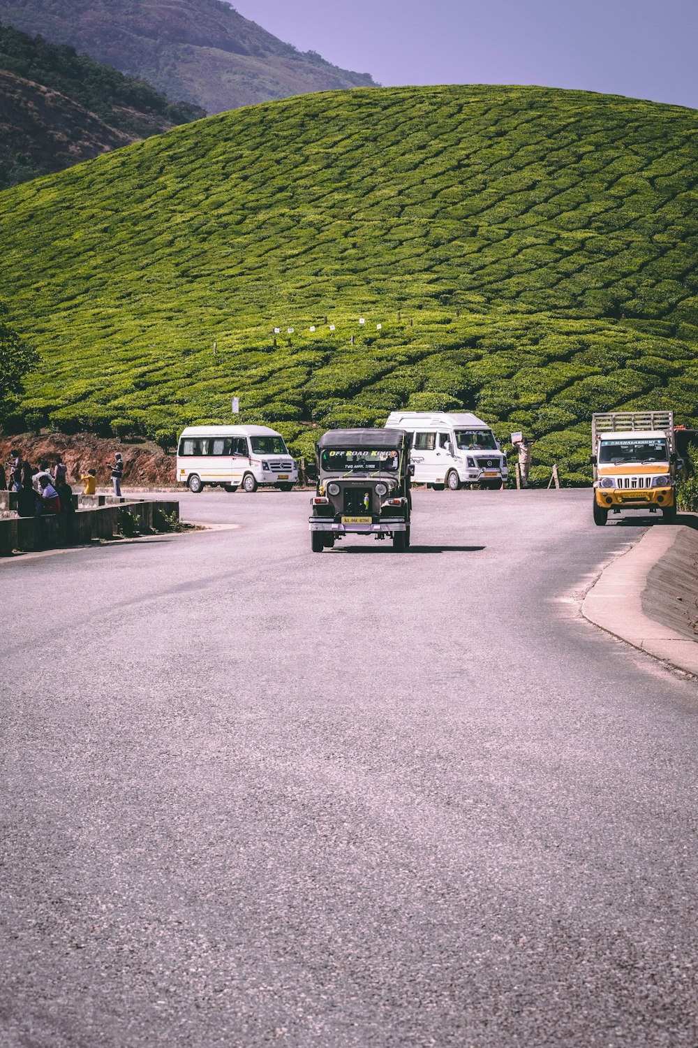 a group of buses driving down a road next to a lush green hillside