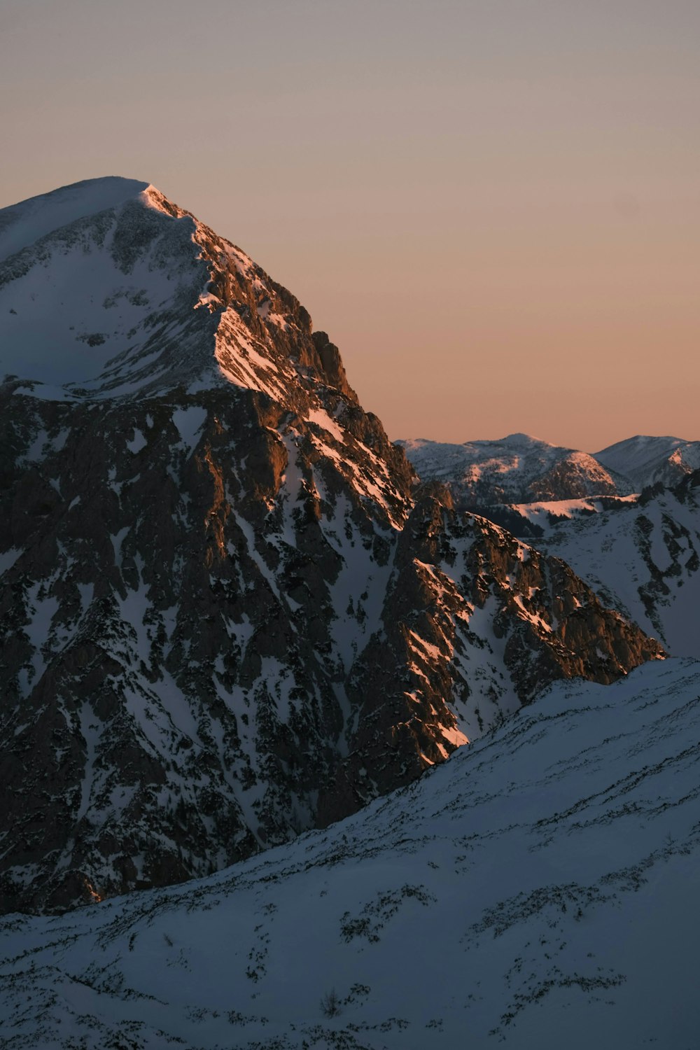 Ein schneebedeckter Berg mit einem rosa Himmel im Hintergrund